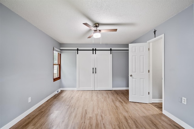 1115 E Herold Ave, Des Moines, IA 50315 - unfurnished bedroom featuring a barn door, wood finished floors, a textured ceiling, and ceiling fan