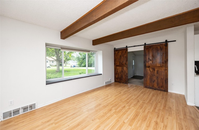 1144 57th St, Des Moines, IA 50311 - unfurnished bedroom with a barn door, light wood-type flooring, beam ceiling, and a textured ceiling