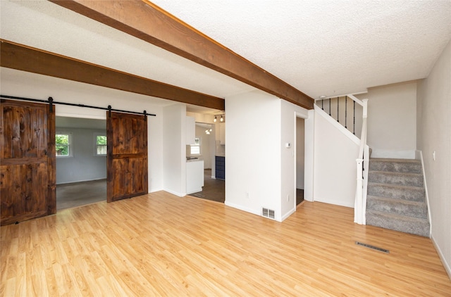1144 57th St, Des Moines, IA 50311 - unfurnished living room featuring a barn door, light wood-type flooring, and stairway