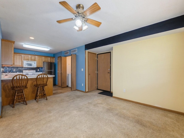 5908 Sutton Pl Unit 1, Urbandale, IA 50322 - kitchen with white microwave, freestanding refrigerator, light colored carpet, a kitchen bar, and a peninsula