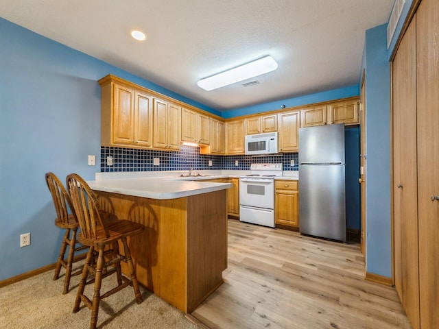 5908 Sutton Pl Unit 1, Urbandale, IA 50322 - kitchen with white appliances, a peninsula, tasteful backsplash, a breakfast bar area, and light countertops