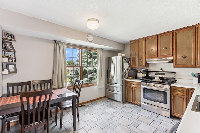 206 Main St, Grinnell, IA 50112 - kitchen with appliances with stainless steel finishes, under cabinet range hood, brown cabinets, light countertops, and backsplash