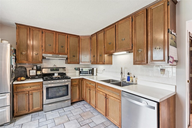 206 Main St, Grinnell, IA 50112 - kitchen with stainless steel appliances, under cabinet range hood, light countertops, brown cabinets, and a textured ceiling