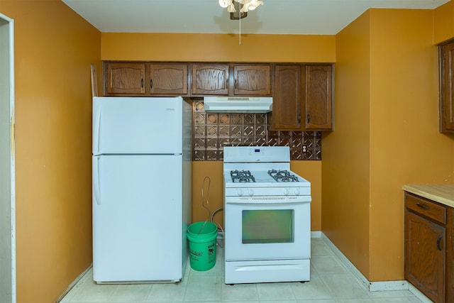 832 E Lacona Ave, Des Moines, IA 50315 - kitchen with white appliances, under cabinet range hood, light tile patterned floors, and brown cabinets
