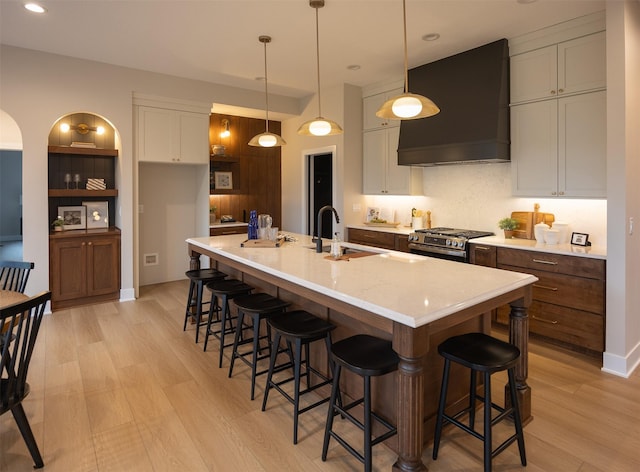 1128 NW 29th Ct, Grimes, IA 50111 - kitchen with wall chimney exhaust hood, light wood-type flooring, stainless steel range with gas cooktop, light countertops, and a breakfast bar