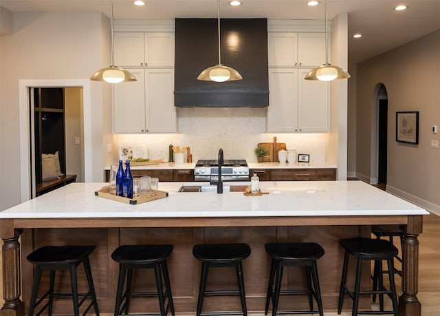 1128 NW 29th Ct, Grimes, IA 50111 - kitchen featuring wall chimney range hood, recessed lighting, a large island with sink, arched walkways, and tasteful backsplash