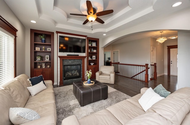 9824 Dunmore Cir, Johnston, IA 50131 - living room featuring arched walkways, a ceiling fan, a tile fireplace, built in features, and a raised ceiling