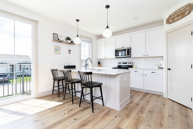 720 Spruce St NW, Bondurant, IA 50035 - kitchen featuring appliances with stainless steel finishes, tasteful backsplash, a peninsula, light wood-type flooring, and white cabinets