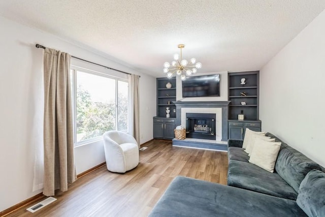 4965 Raintree Dr, West Des Moines, IA 50265 - living area with a chandelier, light wood-style flooring, a textured ceiling, a glass covered fireplace, and built in shelves