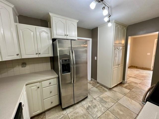 1506 Main St, Adel, IA 50003 - kitchen featuring stainless steel fridge with ice dispenser, light countertops, white cabinets, rail lighting, and tasteful backsplash