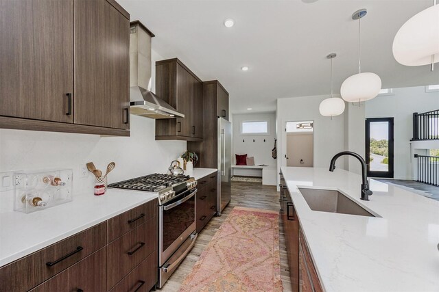 989 65th St, West Des Moines, IA 50266 - kitchen with stainless steel appliances, wall chimney exhaust hood, dark brown cabinets, hanging light fixtures, and light wood-type flooring