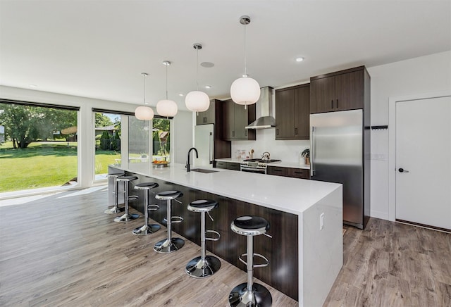 989 65th St, West Des Moines, IA 50266 - kitchen with stainless steel appliances, light wood-style flooring, wall chimney range hood, dark brown cabinets, and light countertops