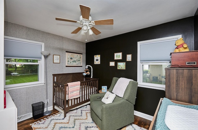 3925 55th St, Des Moines, IA 50310 - bedroom featuring a crib, wood finished floors, a ceiling fan, and wallpapered walls