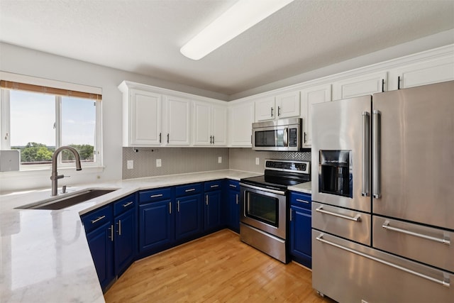 7039 Carey Ct, Johnston, IA 50131 - kitchen with stainless steel appliances, blue cabinets, white cabinetry, light wood finished floors, and decorative backsplash
