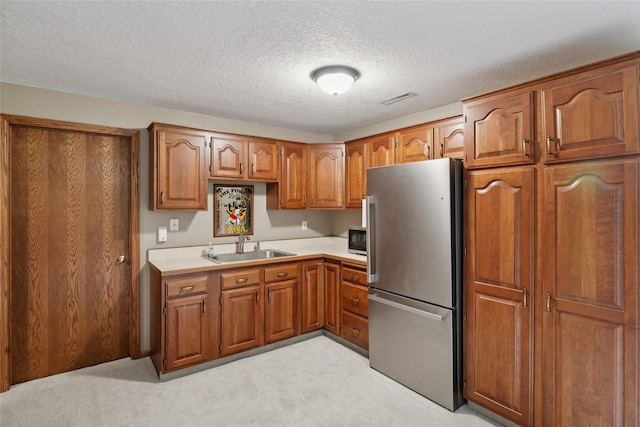 940 High Ave, Newton, IA 50208 - kitchen featuring freestanding refrigerator, brown cabinetry, light colored carpet, a textured ceiling, and light countertops