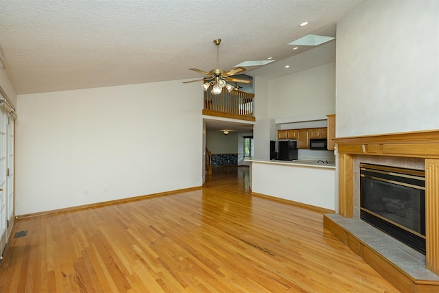 1560 Castlegar Ct, Pleasant Hill, IA 50327 - unfurnished living room with a ceiling fan, light wood-style flooring, lofted ceiling, a tile fireplace, and a textured ceiling