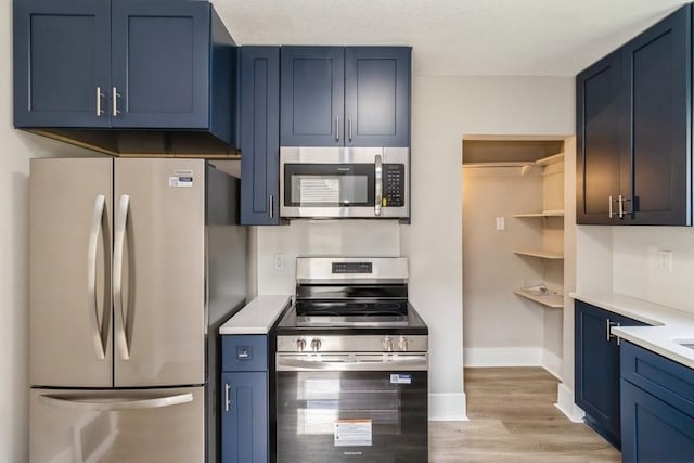 8 E Wall Ave, Des Moines, IA 50315 - kitchen featuring appliances with stainless steel finishes, blue cabinetry, light countertops, and light wood finished floors