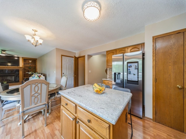 3436 Valley View Dr, West Des Moines, IA 50265 - kitchen featuring stainless steel fridge with ice dispenser, a kitchen island, light wood-style floors, a textured ceiling, and a fireplace