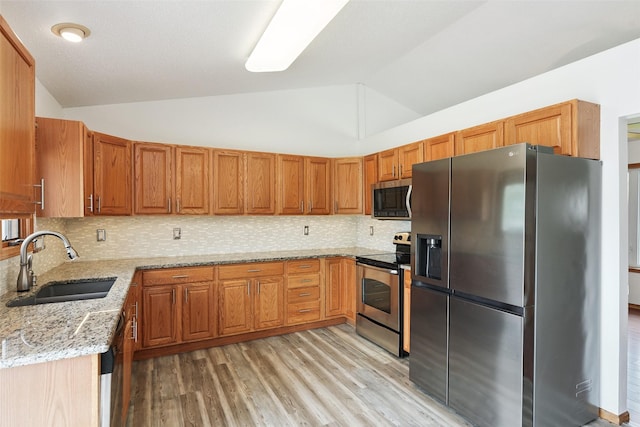 2907 E 43rd St, Des Moines, IA 50317 - kitchen featuring stainless steel appliances, vaulted ceiling, light stone countertops, light wood-style flooring, and brown cabinetry