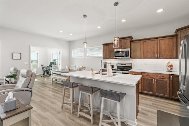 8932 Mockingbird Dr, West Des Moines, IA 50266 - kitchen featuring appliances with stainless steel finishes, a breakfast bar area, light countertops, decorative backsplash, and light wood-type flooring