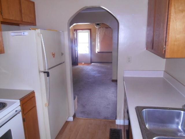 702 Woodbury St, Marshalltown, IA 50158 - kitchen with arched walkways, brown cabinets, light carpet, and freestanding refrigerator