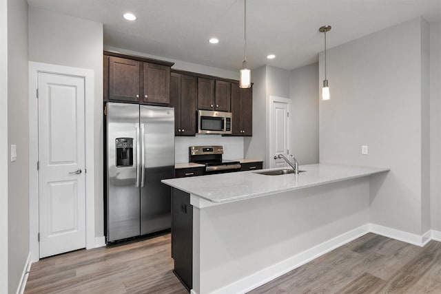 15321 Goldenrod Dr, Urbandale, IA 50323 - kitchen featuring appliances with stainless steel finishes, light wood-style flooring, dark brown cabinets, a peninsula, and tasteful backsplash