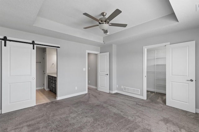 15321 Goldenrod Dr, Urbandale, IA 50323 - unfurnished bedroom with a tray ceiling, carpet flooring, a barn door, a walk in closet, and a closet