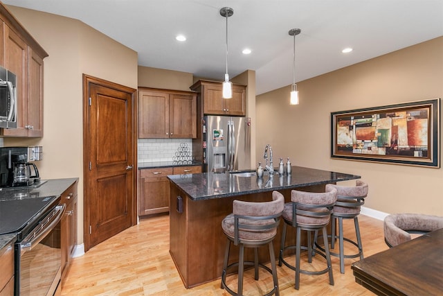 1592 SE Blackthorne Dr, Waukee, IA 50263 - kitchen featuring stainless steel appliances, an island with sink, dark stone counters, a kitchen breakfast bar, and tasteful backsplash