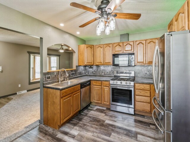 4518 SE 6th St, Des Moines, IA 50315 - kitchen with stainless steel appliances, a ceiling fan, dark countertops, decorative backsplash, and arched walkways