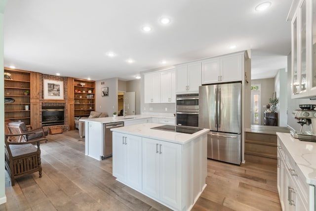 3124 Greenwood Rd, Ames, IA 50014 - kitchen with appliances with stainless steel finishes, a peninsula, a fireplace, light wood-style floors, and white cabinetry