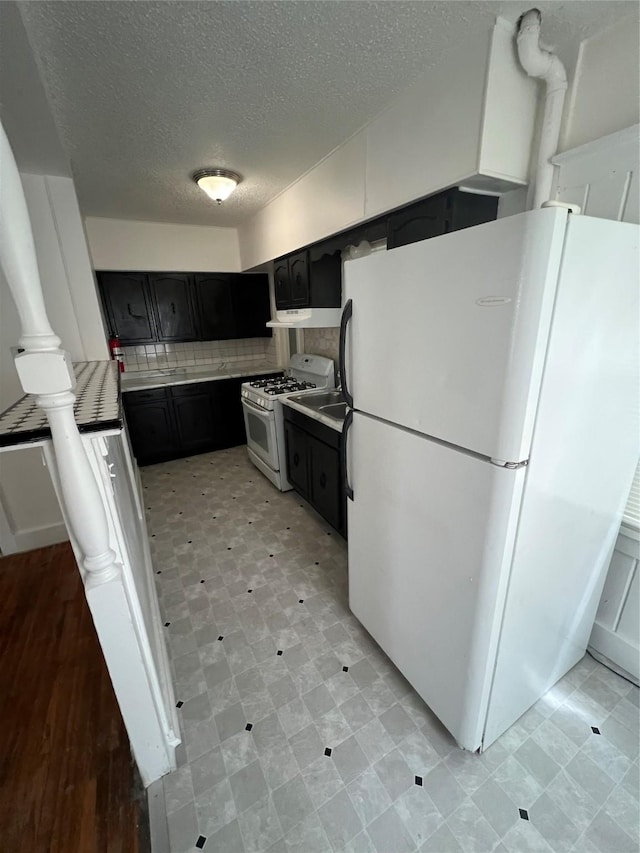 3618 Dubuque Ave, Des Moines, IA 50317 - kitchen with white appliances, dark cabinets, a textured ceiling, light countertops, and under cabinet range hood