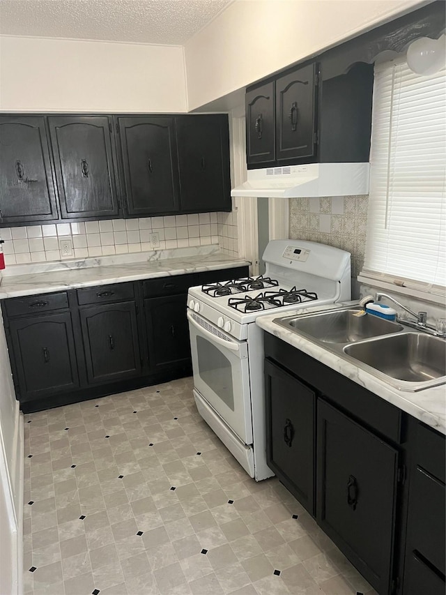 3618 Dubuque Ave, Des Moines, IA 50317 - kitchen with white range with gas stovetop, under cabinet range hood, dark cabinets, backsplash, and light countertops