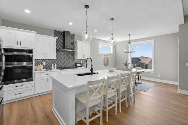 17736 Hammontree Dr, Clive, IA 50325 - kitchen with wall chimney exhaust hood, appliances with stainless steel finishes, a kitchen island with sink, backsplash, and light wood finished floors