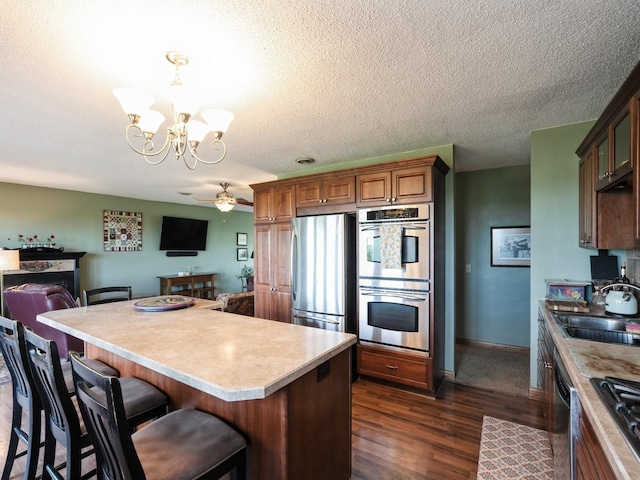 1246 N 75th Ave W, Newton, IA 50208 - kitchen featuring stainless steel appliances, a chandelier, dark wood-style floors, a ceiling fan, and a breakfast bar