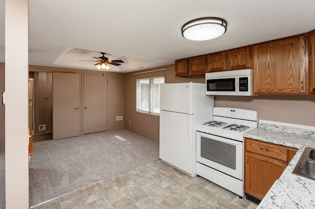 401 NW 50th Pl, Des Moines, IA 50313 - kitchen with white appliances, ceiling fan, brown cabinets, light countertops, and light colored carpet