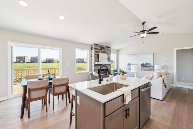 4422 NW Olivia Ln, Ankeny, IA 50023 - kitchen featuring stainless steel dishwasher, open floor plan, light wood finished floors, a stone fireplace, and a center island with sink