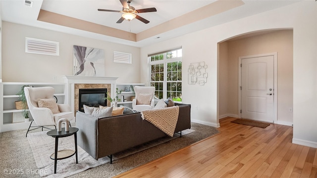 2811 SW Westview Ln, Ankeny, IA 50023 - living room featuring a tray ceiling, ceiling fan, a tile fireplace, light wood-style floors, and arched walkways