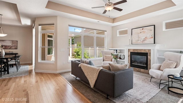 2811 SW Westview Ln, Ankeny, IA 50023 - living room featuring a tray ceiling, a ceiling fan, a tiled fireplace, and light wood-style flooring