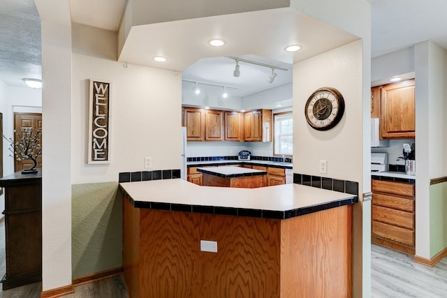 201 E 1st St, Woodward, IA 50276 - kitchen featuring light wood-type flooring, brown cabinets, white appliances, a peninsula, and track lighting