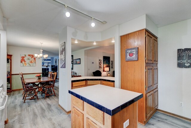 201 E 1st St, Woodward, IA 50276 - kitchen featuring light wood-style flooring, a chandelier, a kitchen island, rail lighting, and tile countertops