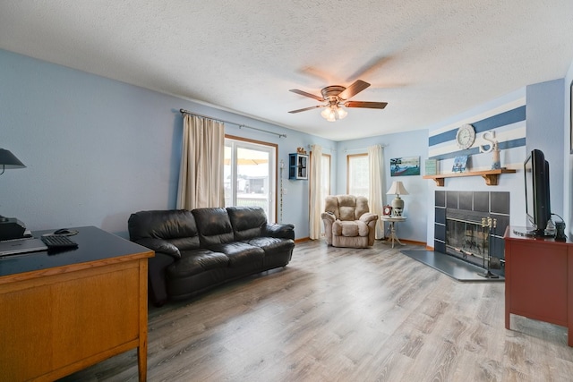 201 E 1st St, Woodward, IA 50276 - living room with ceiling fan, a tiled fireplace, light wood finished floors, a textured ceiling, and an office area