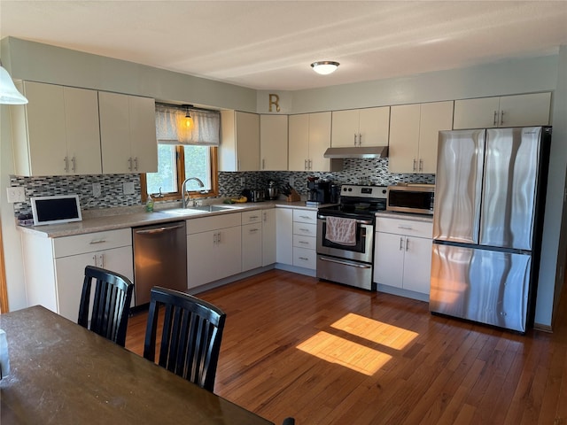 410 N 6th St, Winterset, IA 50273 - kitchen with stainless steel appliances, under cabinet range hood, tasteful backsplash, dark wood-style floors, and white cabinets
