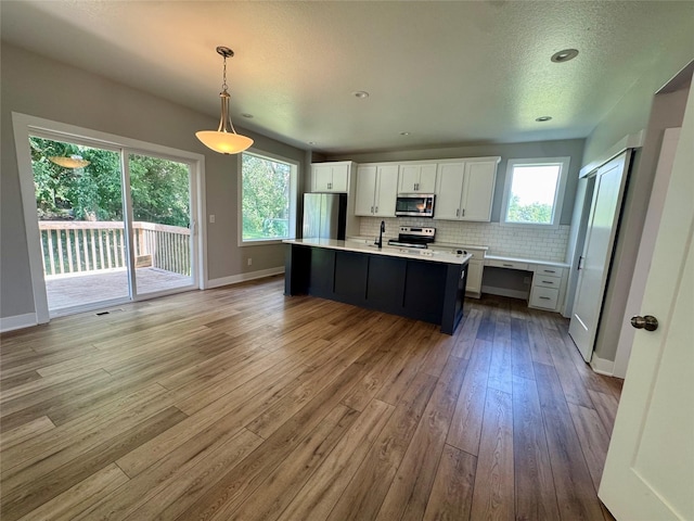 10009 Powell Ave, Johnston, IA 50131 - kitchen featuring appliances with stainless steel finishes, light countertops, hardwood / wood-style flooring, white cabinetry, and tasteful backsplash