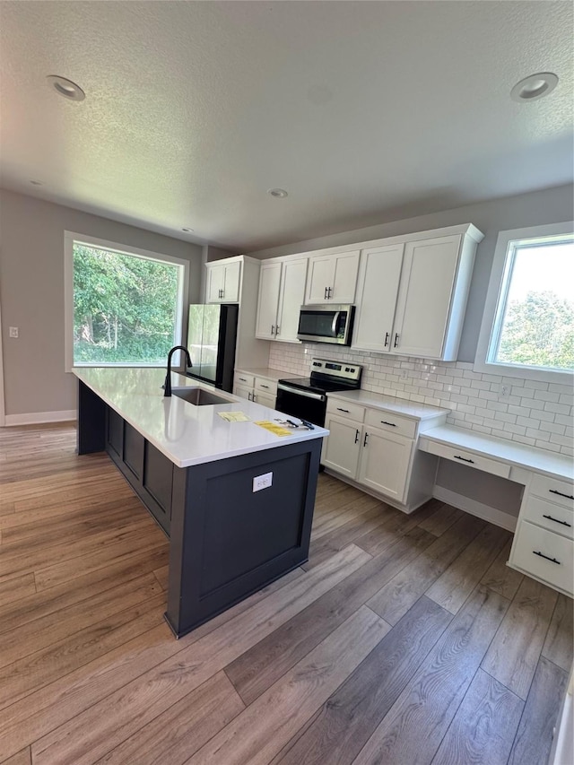 10009 Powell Ave, Johnston, IA 50131 - kitchen with stainless steel appliances, tasteful backsplash, white cabinets, a center island with sink, and a textured ceiling