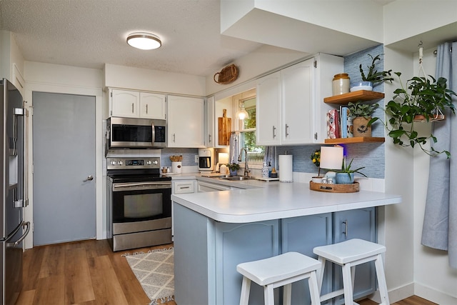 1506 S 14th St, Adel, IA 50003 - kitchen with stainless steel appliances, a peninsula, white cabinetry, backsplash, and wood finished floors