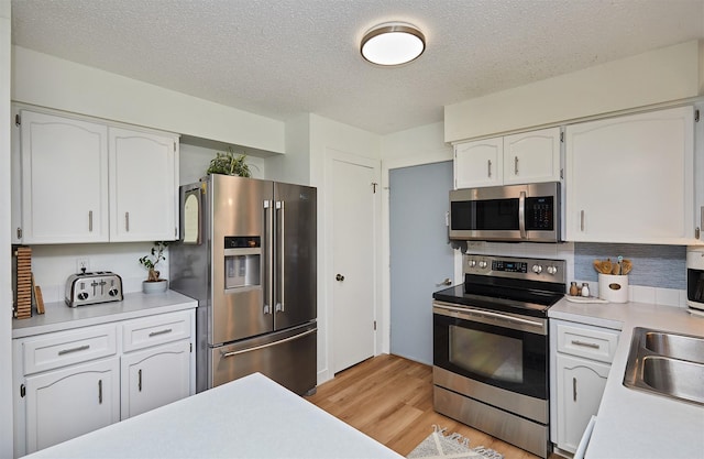 1506 S 14th St, Adel, IA 50003 - kitchen with appliances with stainless steel finishes, light countertops, white cabinetry, light wood-style floors, and a textured ceiling