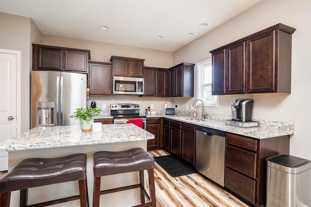 303 SE 14th St, Grimes, IA 50111 - kitchen featuring appliances with stainless steel finishes, dark brown cabinetry, light wood-type flooring, a center island, and light stone countertops