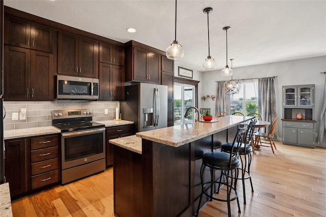 1609 NW Prairie Creek Dr, Grimes, IA 50111 - kitchen featuring appliances with stainless steel finishes, dark brown cabinets, a kitchen bar, tasteful backsplash, and light wood finished floors