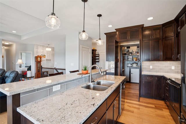 1609 NW Prairie Creek Dr, Grimes, IA 50111 - kitchen featuring appliances with stainless steel finishes, light wood-style flooring, dark brown cabinetry, tasteful backsplash, and light stone countertops