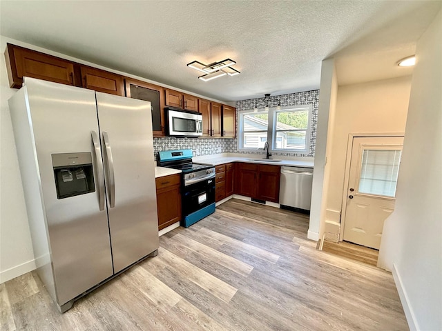2011 E 23rd St, Des Moines, IA 50317 - kitchen featuring stainless steel appliances, light wood-style floors, backsplash, light countertops, and a textured ceiling